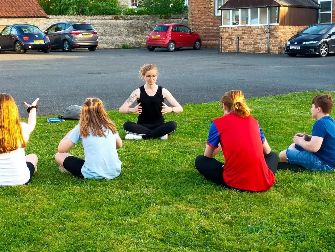 Sat upon lush green grass, Hannah is teaching a group of teens how to meditate.
